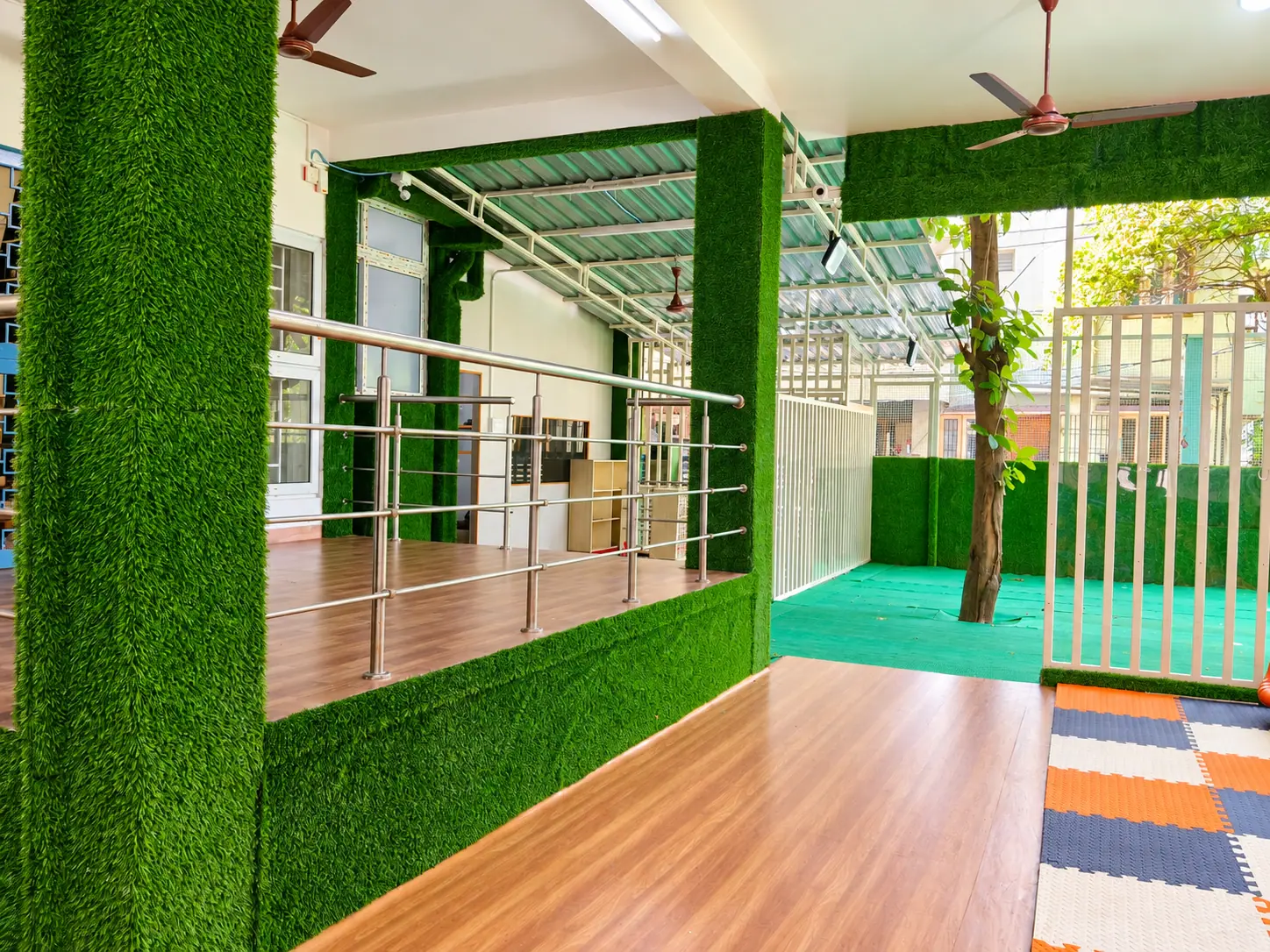Turf-lined corridor with steel railing connecting the classroom block to the outdoor play deck