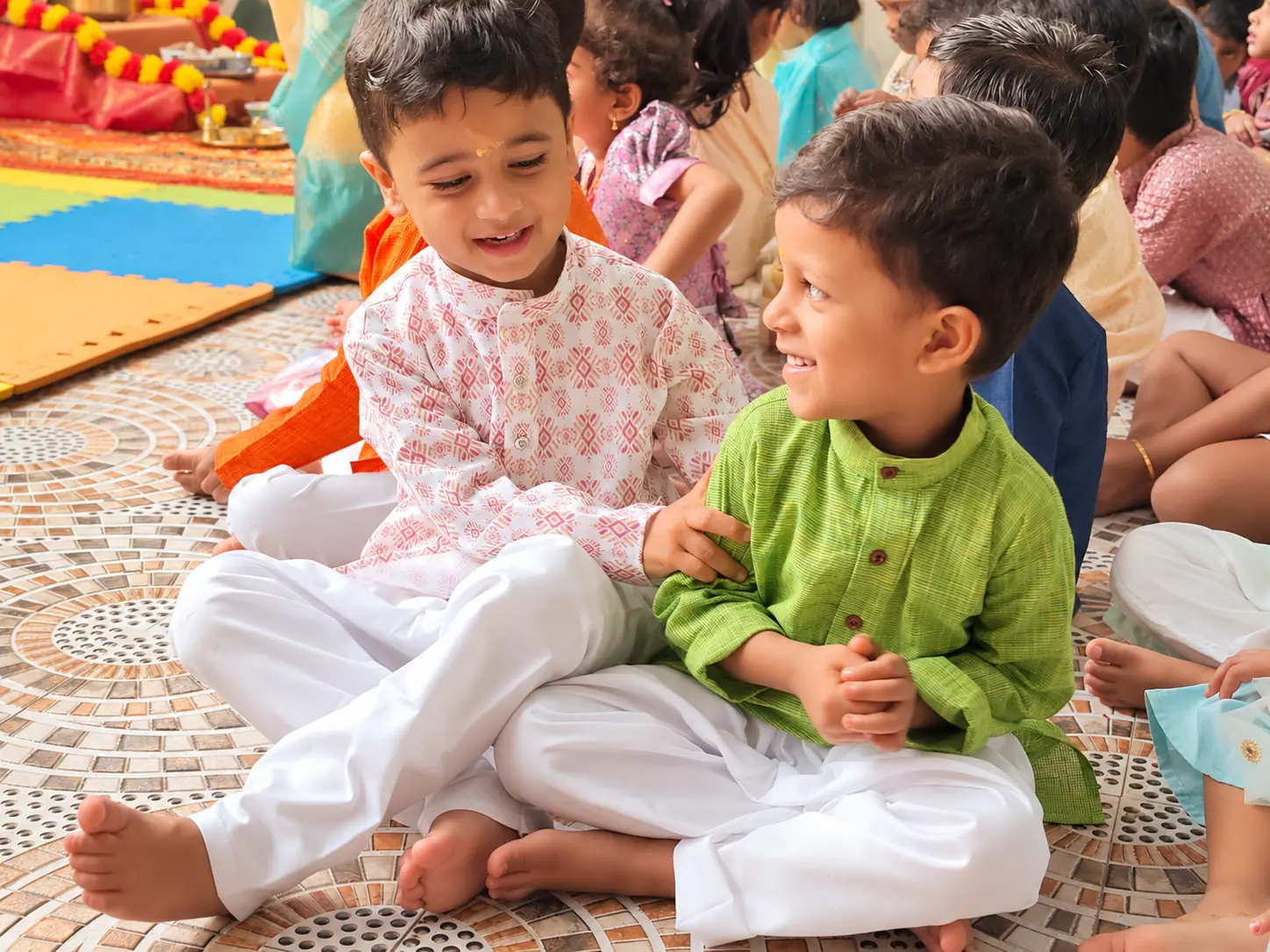 Two preschool boys in traditional attire chatting during independent, child-led activity time at Little Pumpkien Montessori