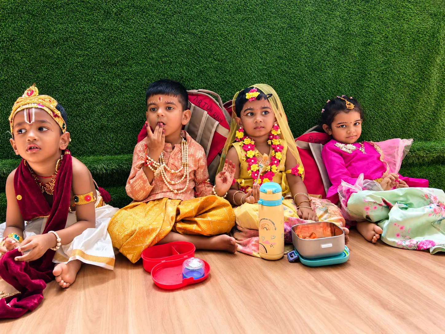 Children in colourful traditional Janmashtami costumes sitting together with their lunch boxes