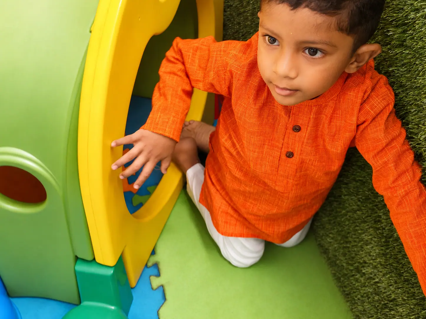 A preschooler using both hands to explore an indoor play structure, building fine motor skills and coordination at Little Pumpkien