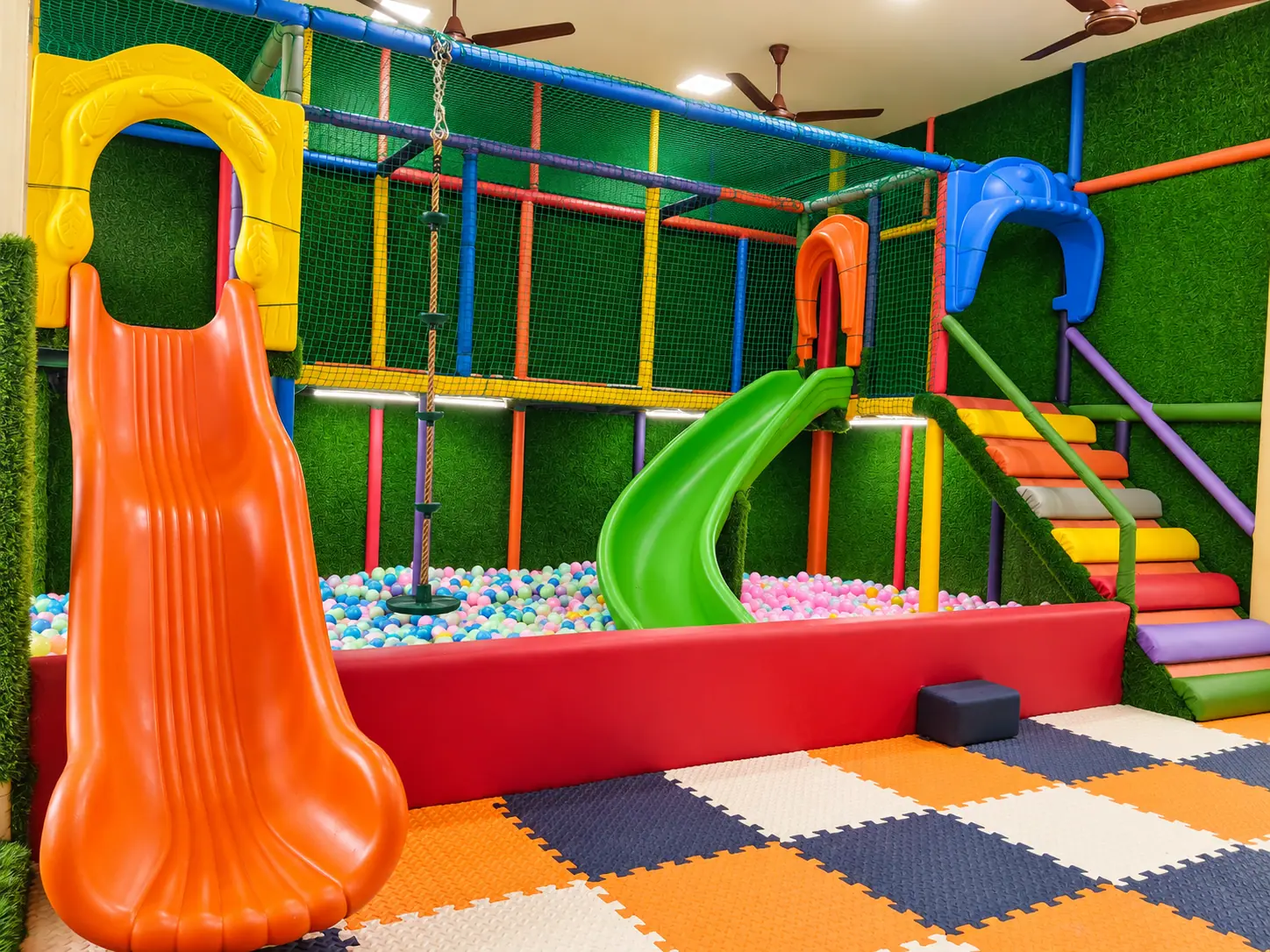 Multi-level indoor soft-play structure with a ball pit and orange and green slides